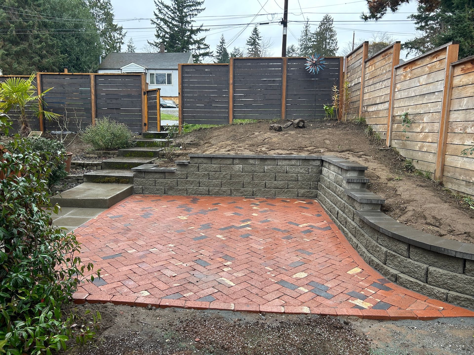 Backyard patio with red brick paving, stone steps, and wood fencing around a raised garden bed
