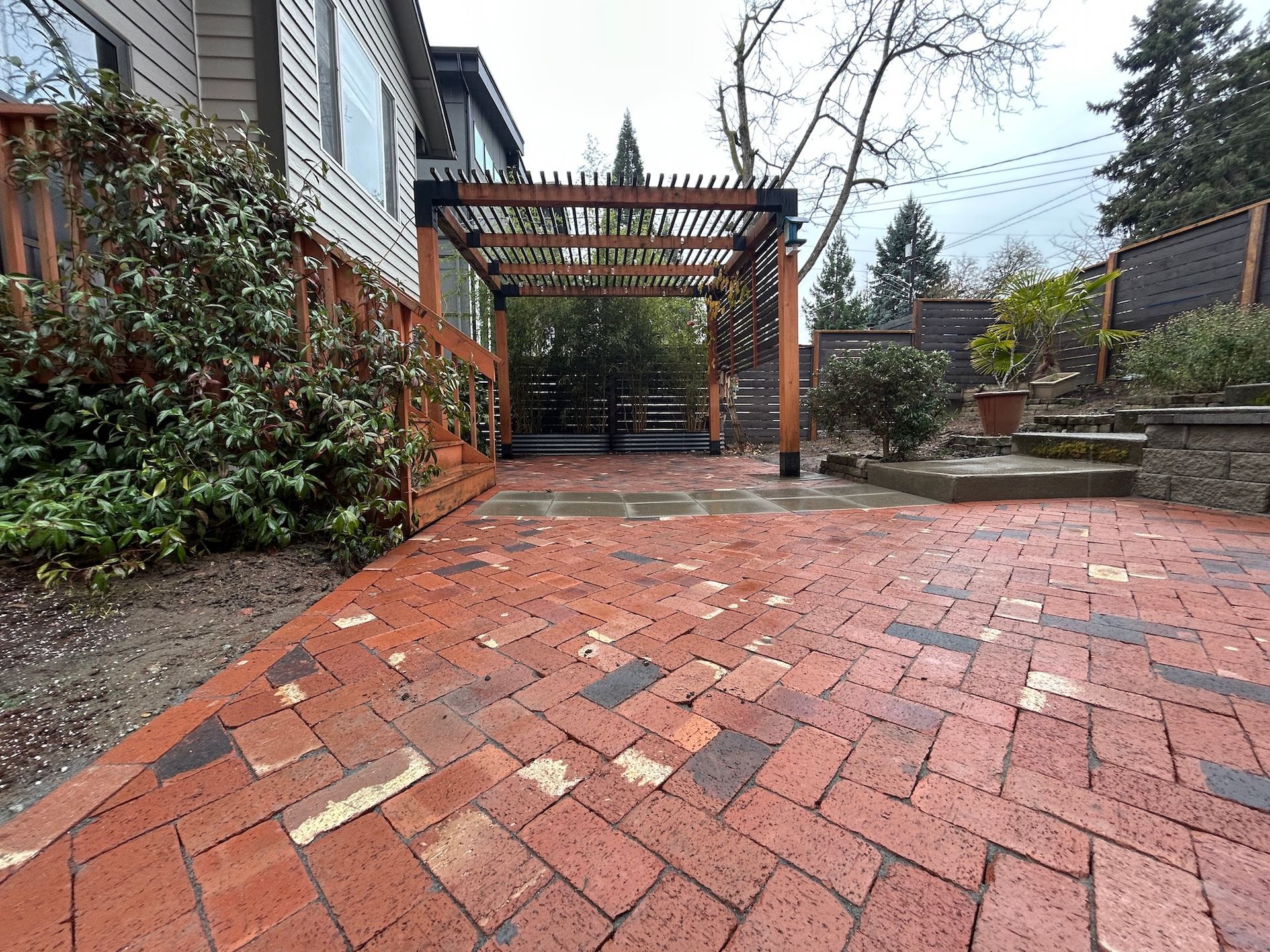 Brick patio with a wooden pergola, steps, and garden landscaping beside a house