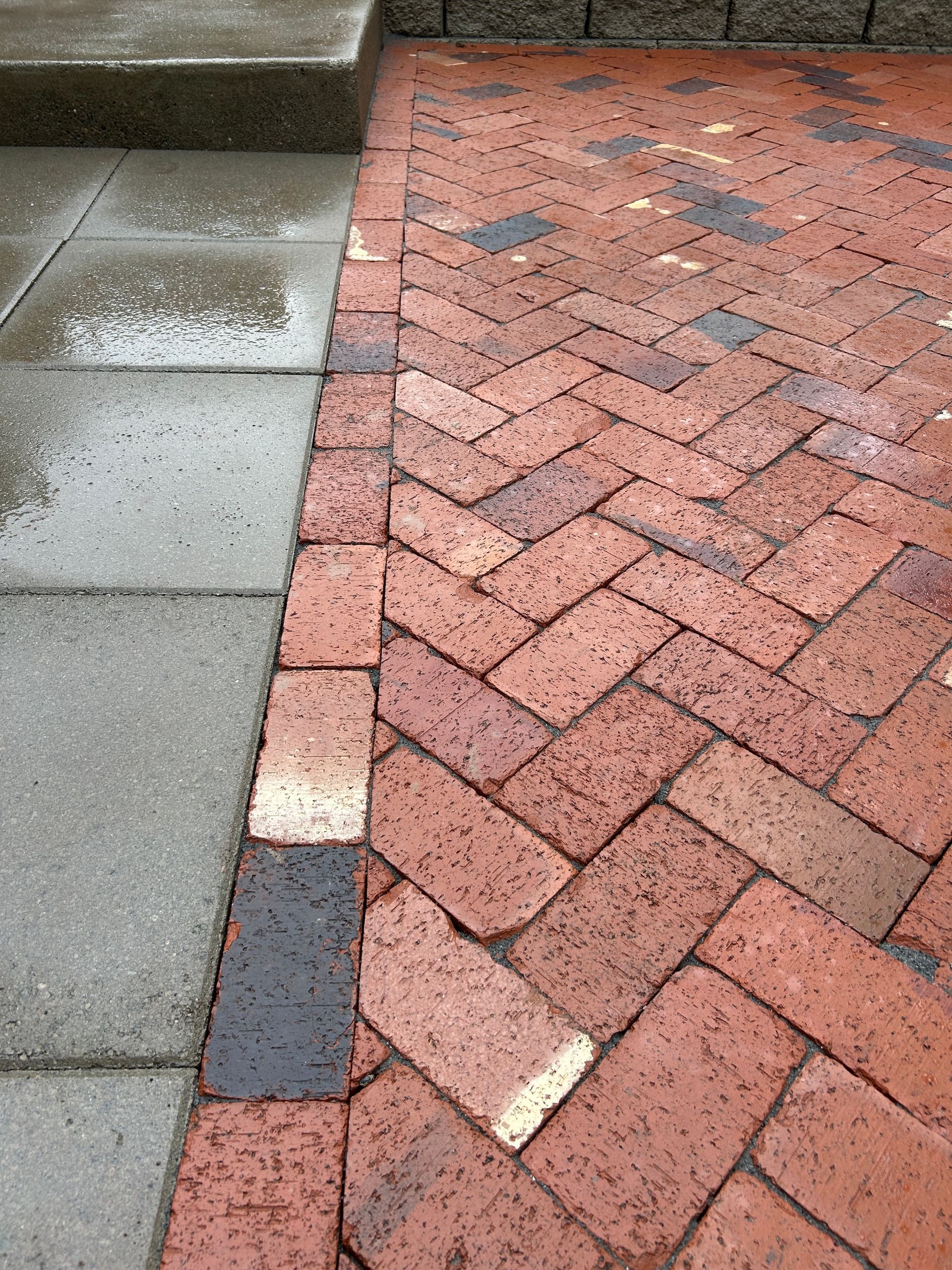 Wet sidewalk next to red brick paving with chipped edge and scattered debris