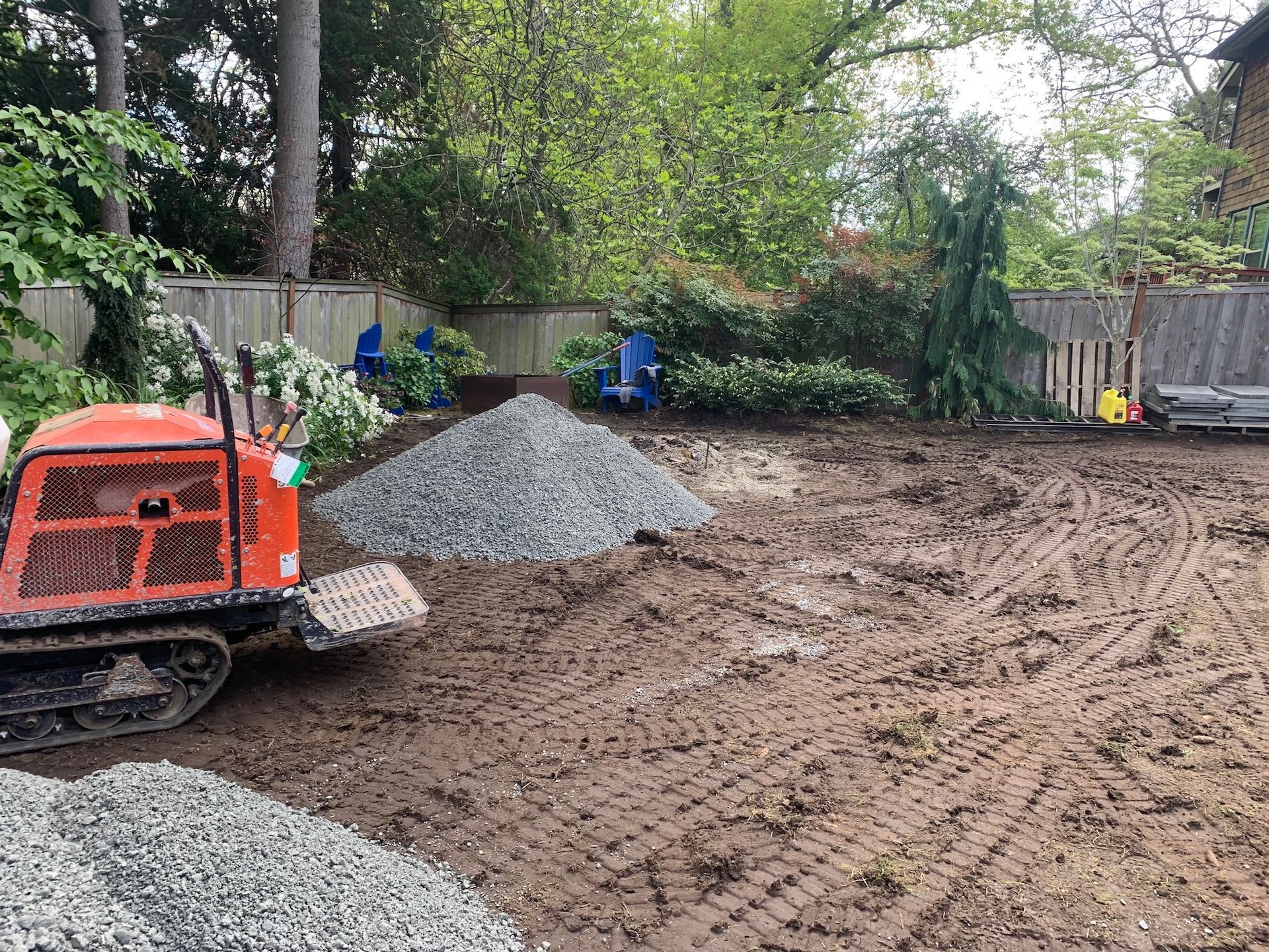 Small excavator on a muddy construction site with gravel piles and trees in the background