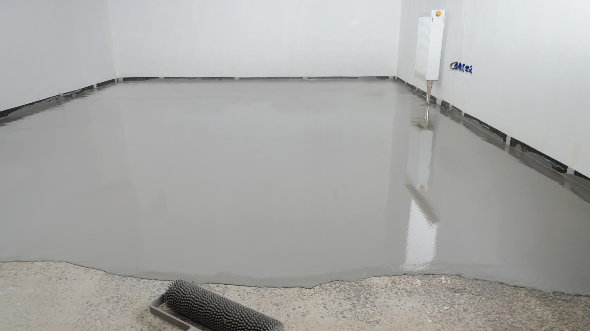 Newly poured, glossy gray epoxy floor in a room with white walls, a brush in the foreground.