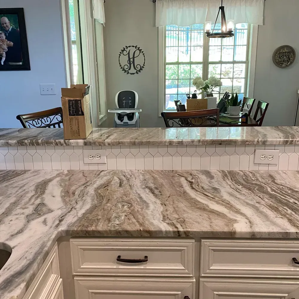 Kitchen with white cabinets, marble countertops, and a dining area visible in the background.