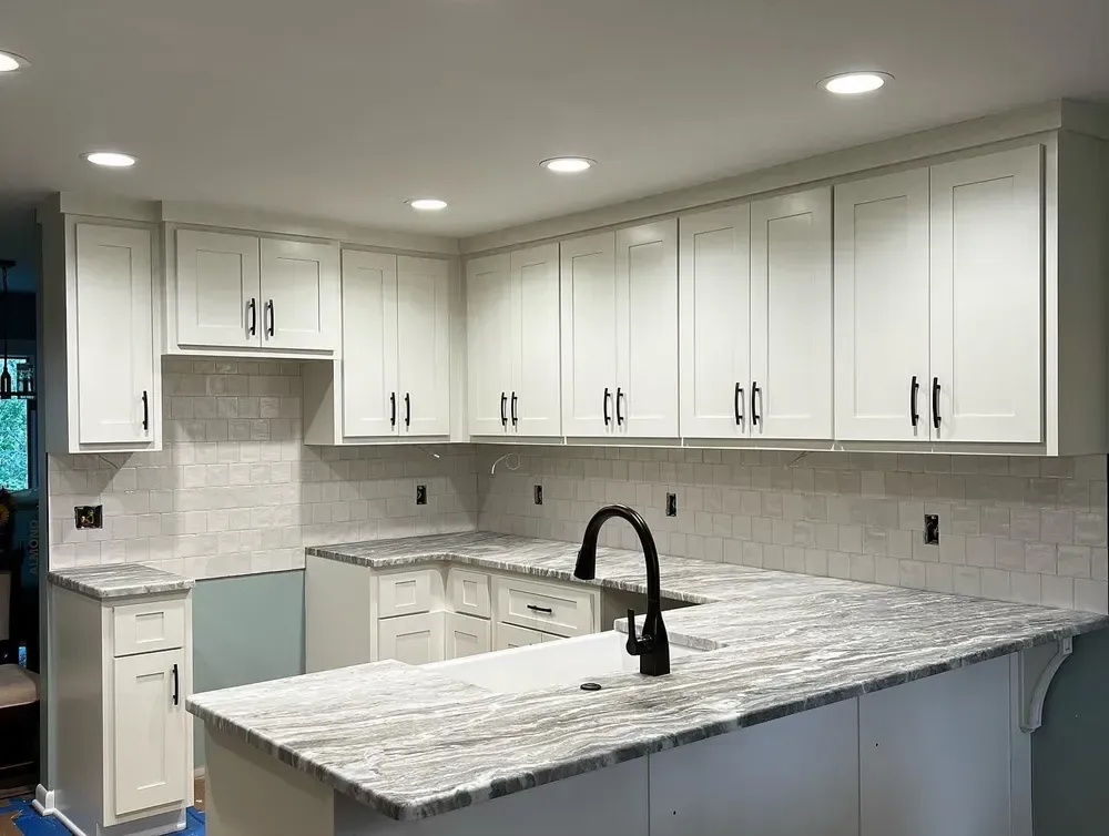 White kitchen with light countertops, black faucet, and white cabinets.