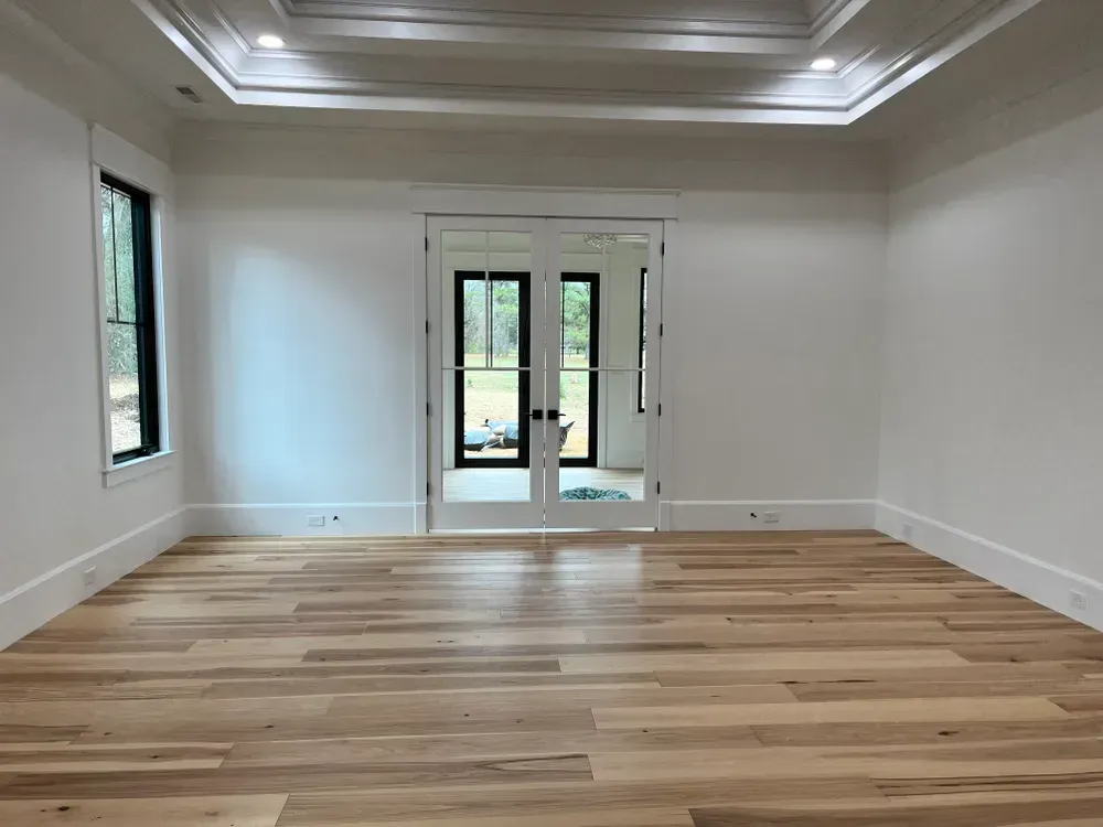 Empty room with hardwood floors, white walls, black-framed doors and windows.
