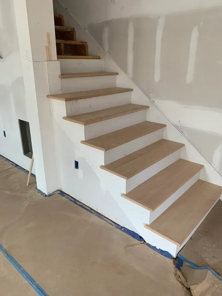 Staircase under construction: wooden steps, white risers, plaster walls, and unfinished lower floor.