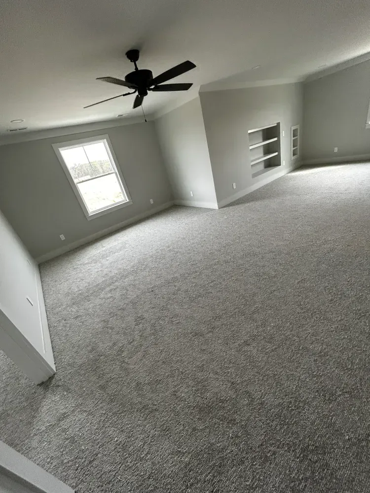 Empty room with gray carpet, ceiling fan, and built-in shelving.