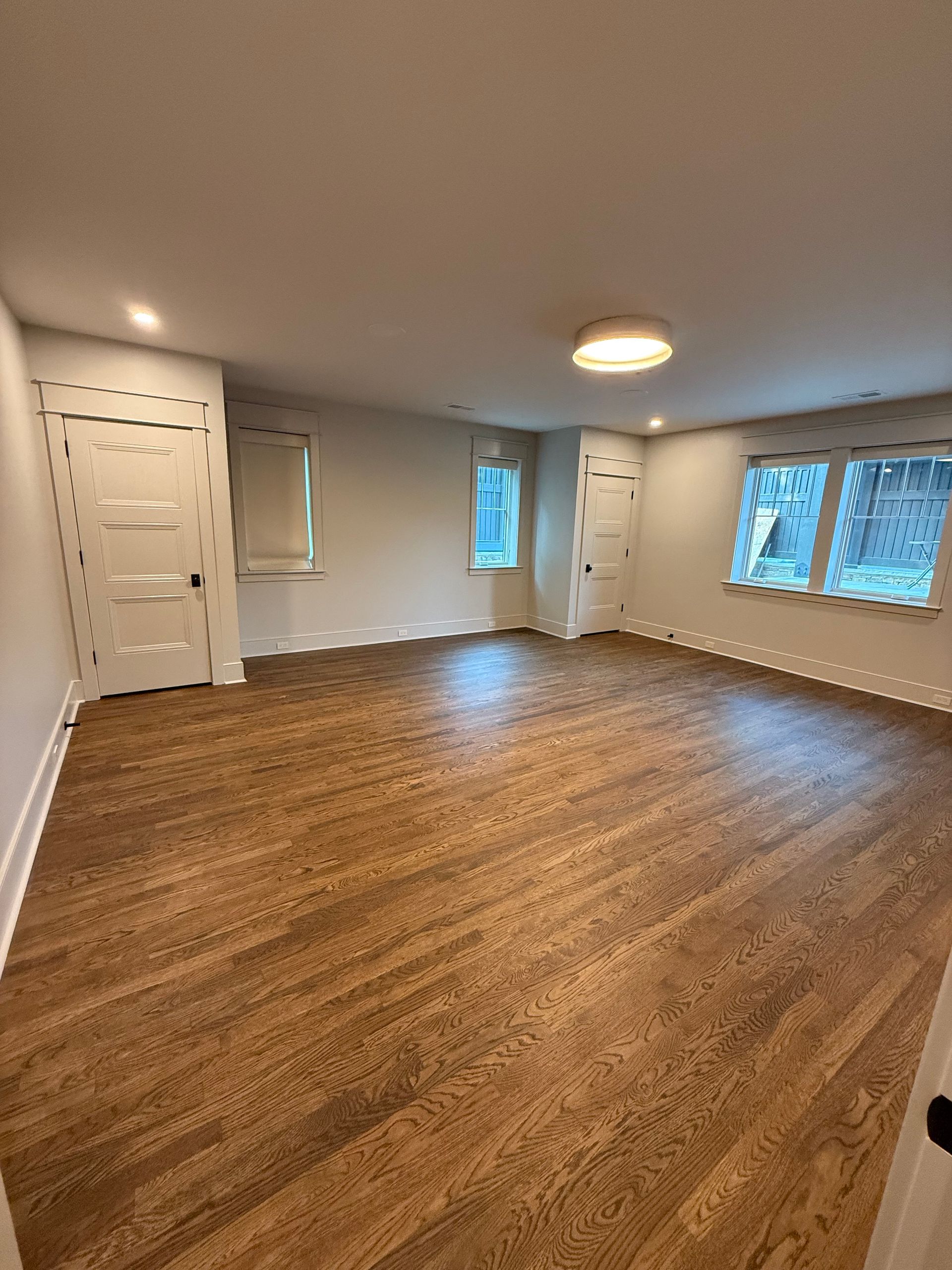 Empty room with hardwood floors, white walls, two windows, and two doors.