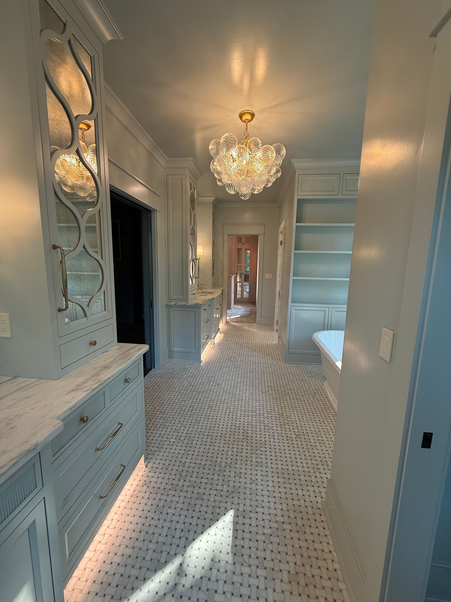 A long, light blue hallway with patterned flooring, built-in cabinets, and a chandelier.