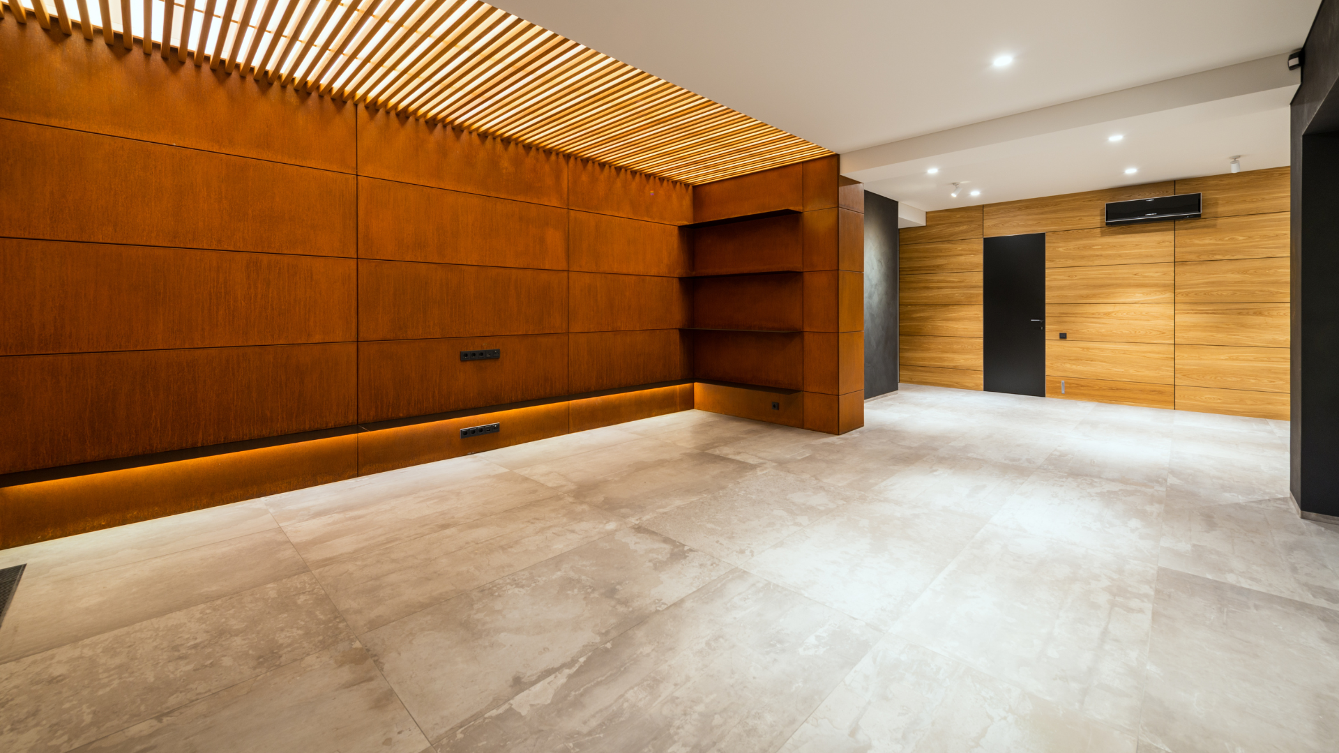 Empty modern room with wooden paneling, recessed shelves, and light gray tile flooring.