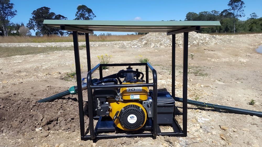A Yellow Pump Is Sitting Under A Canopy In A Field — Manning Valley Pumps And Irrigation In Forster, NSW