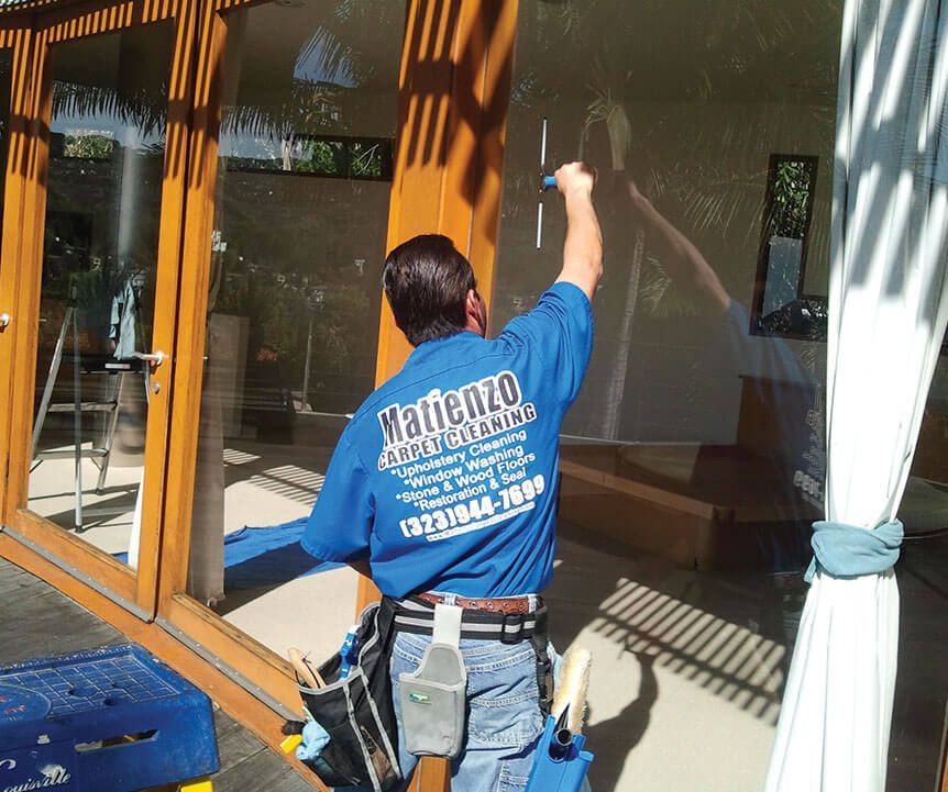 A man wearing a blue shirt that says manenza is cleaning a window