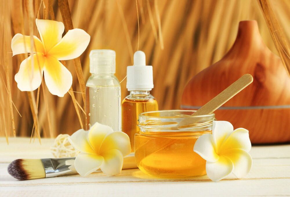 A Jar of Honey is Surrounded by Bottles of Essential Oils and Flowers — Aria Skin & Beauty in Gympie, QLD