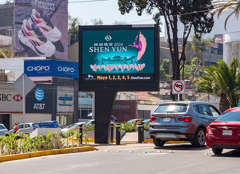 Cartel publicitario de la actuación de Shen Yun. Otros carteles de Choppo, HSBC y AT&T. Coches aparcados en la calle.
