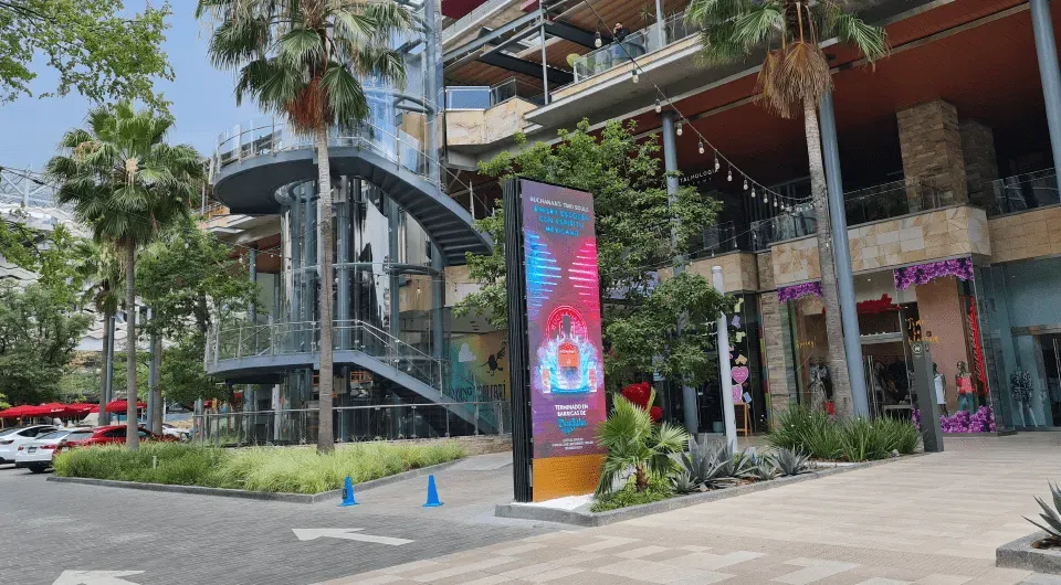 Moderno centro comercial al aire libre con señalización, escalera de caracol y palmeras.