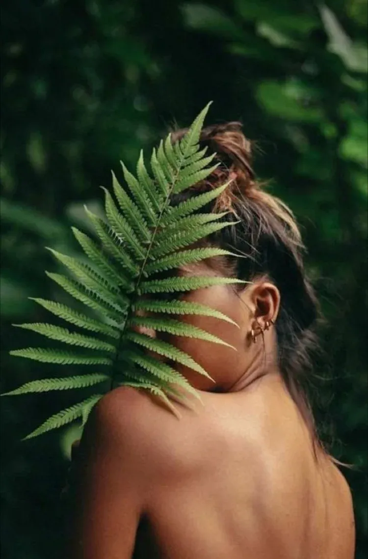 Woman partially hidden behind a large fern in a lush green forest