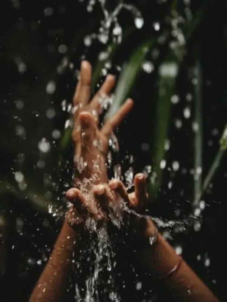 Hands raised under splashing water in a dark setting