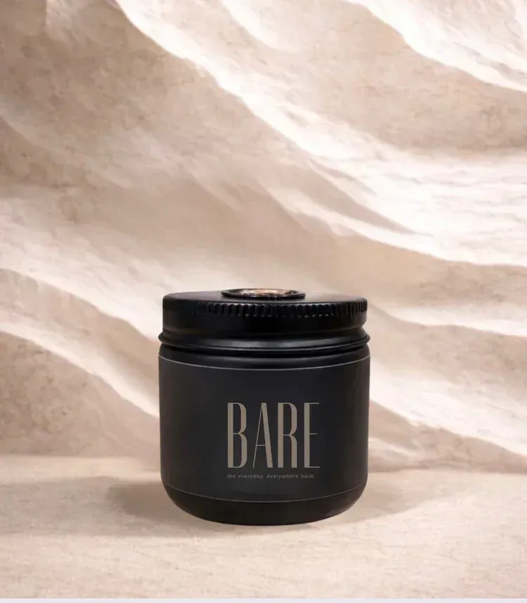 Black cosmetic spray bottle standing on sand against a wavy beige background