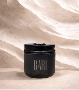 Black cosmetic bottle standing on a sandy beige textured background.