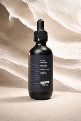 Black dropper bottle of skincare serum on a beige stone surface against a textured backdrop.