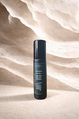 Black cosmetic bottle standing on a sandy beige textured background.