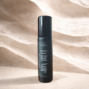 Black cosmetic spray bottle standing on sand against a wavy beige background