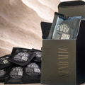 Black snack pouches stacked beside an open black gift box on a beige textured surface