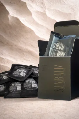 Black gift box and pouches of snacks on a light stone surface with textured background