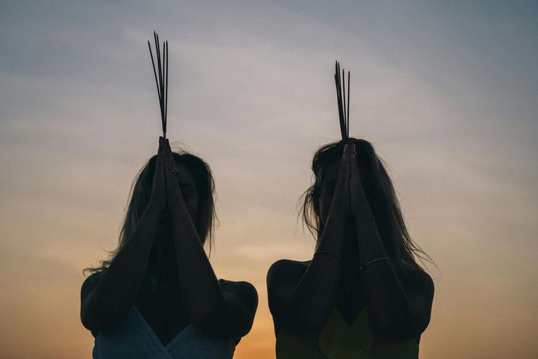 Silhouetted person holding hands overhead at sunset with a tall feathered headdress