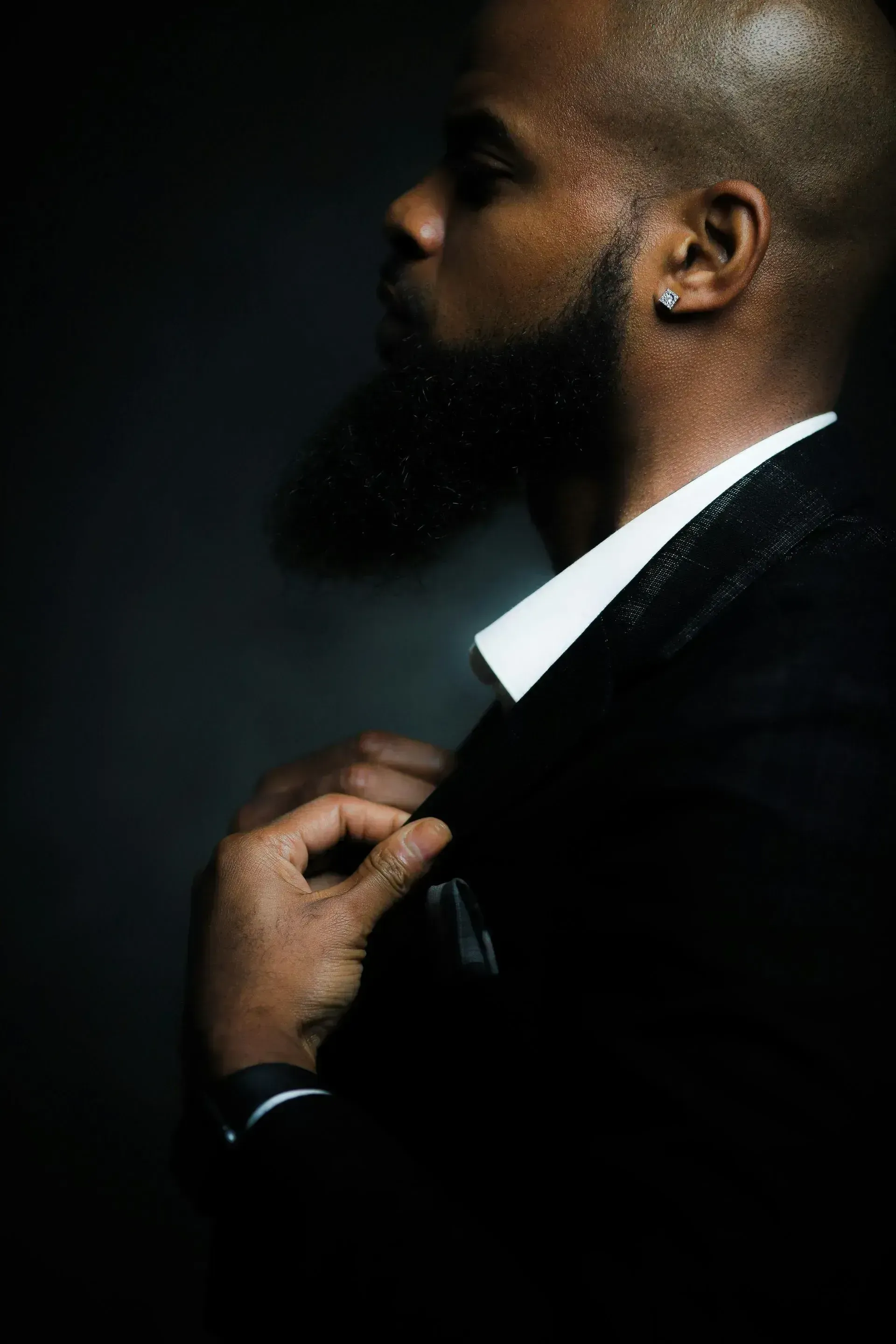Profile of a man in a dark suit adjusting his collar against a dark background