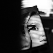 Black-and-white close-up of a face seen through a narrow gap, with a hand partially covering one eye.