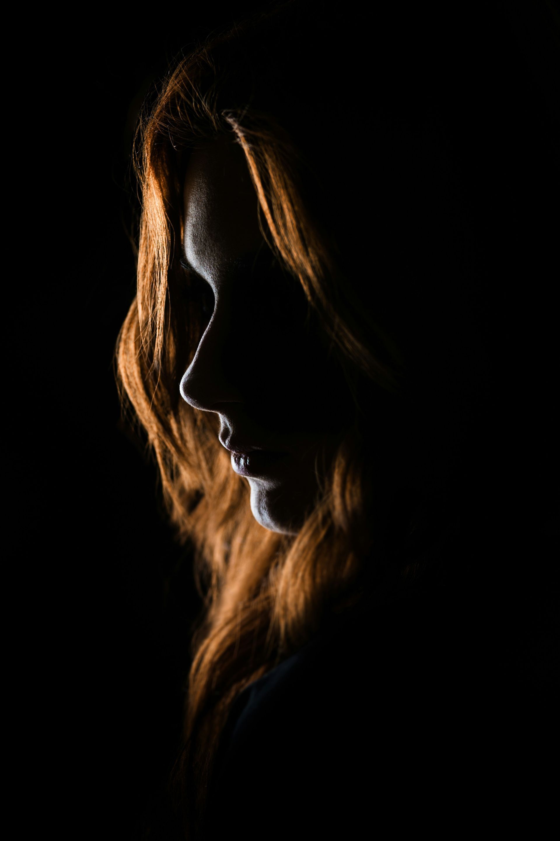 Side-lit profile of a person with long red hair against a black background