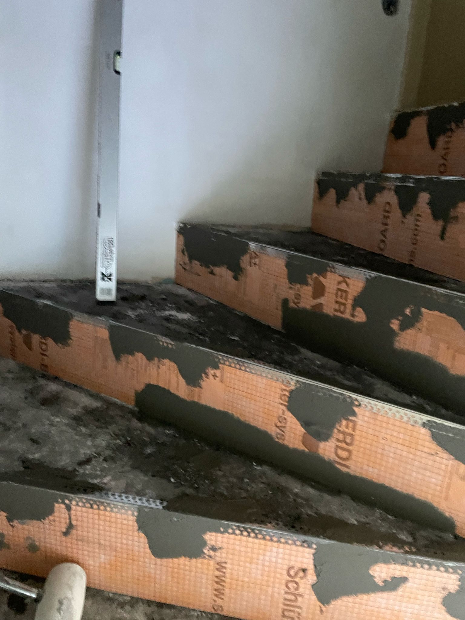 Poškozené schody ve výstavbě s odkrytou oranžovou izolací a tmavými nečistotami na schodech