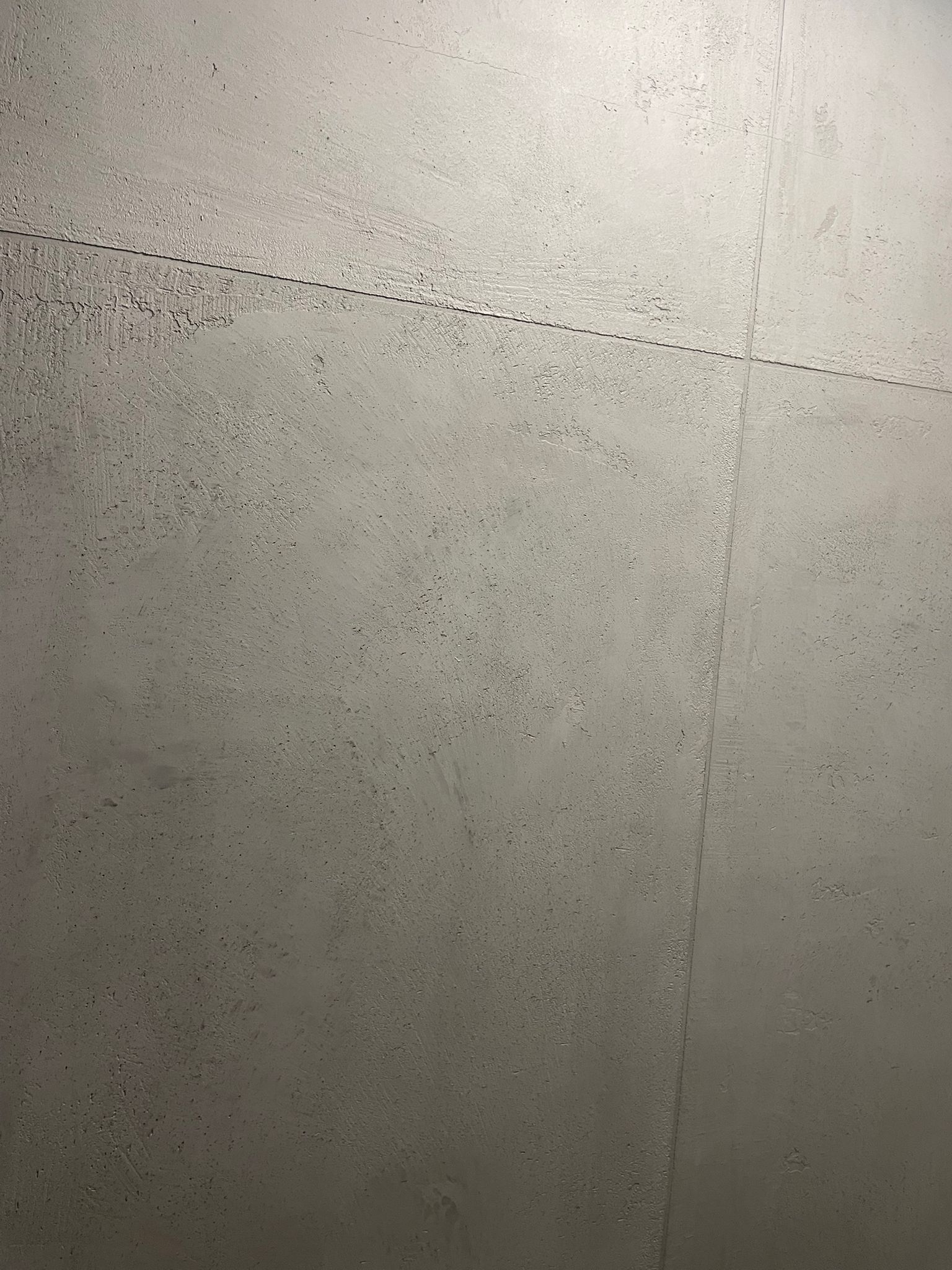 Detail šedého texturovaného povrchu se svislým švem a rozptýlenými tmavými skvrnami