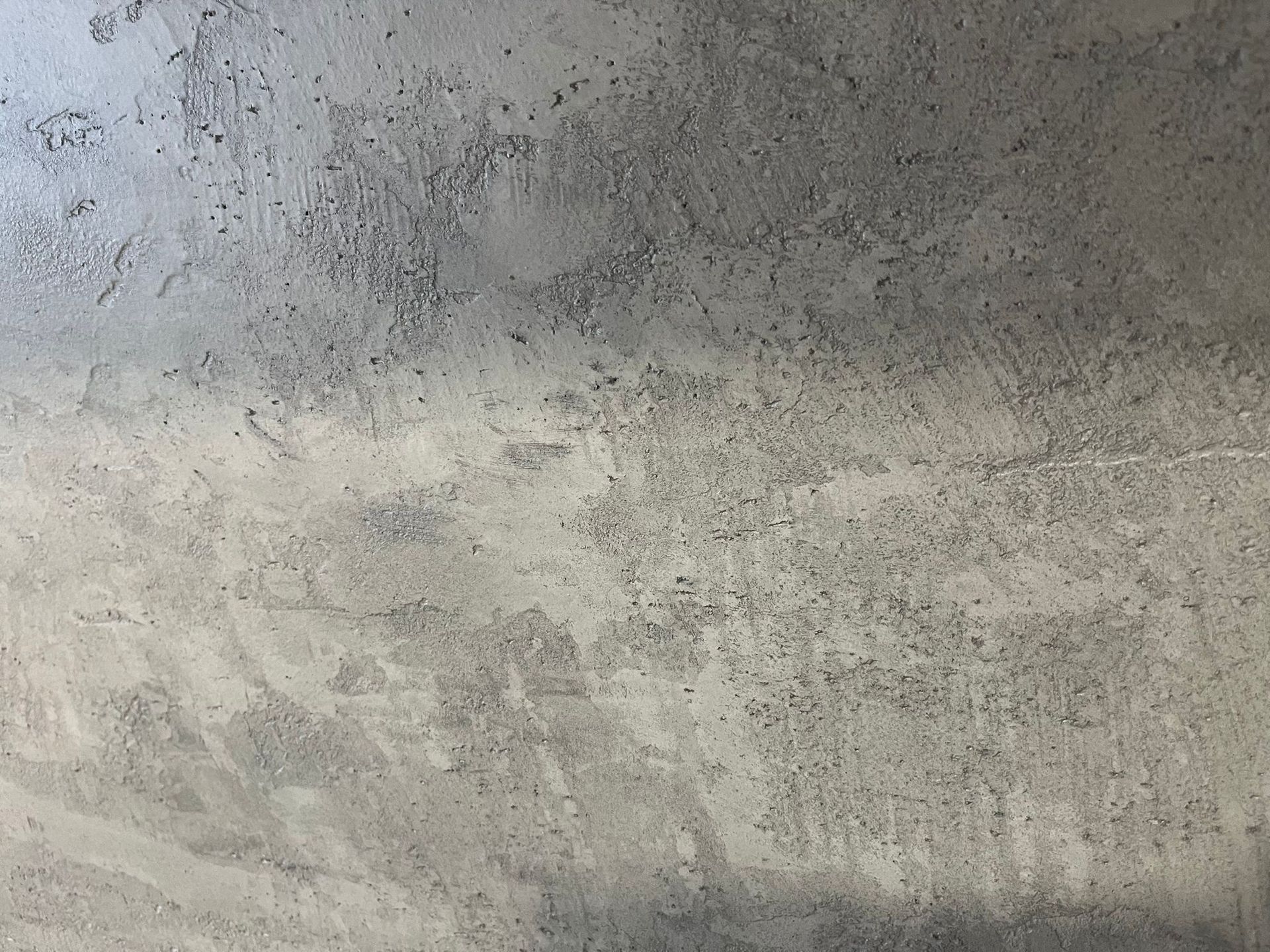 Šedá texturovaná betonová stěna se skvrnami a drsným, skvrnitým povrchem.