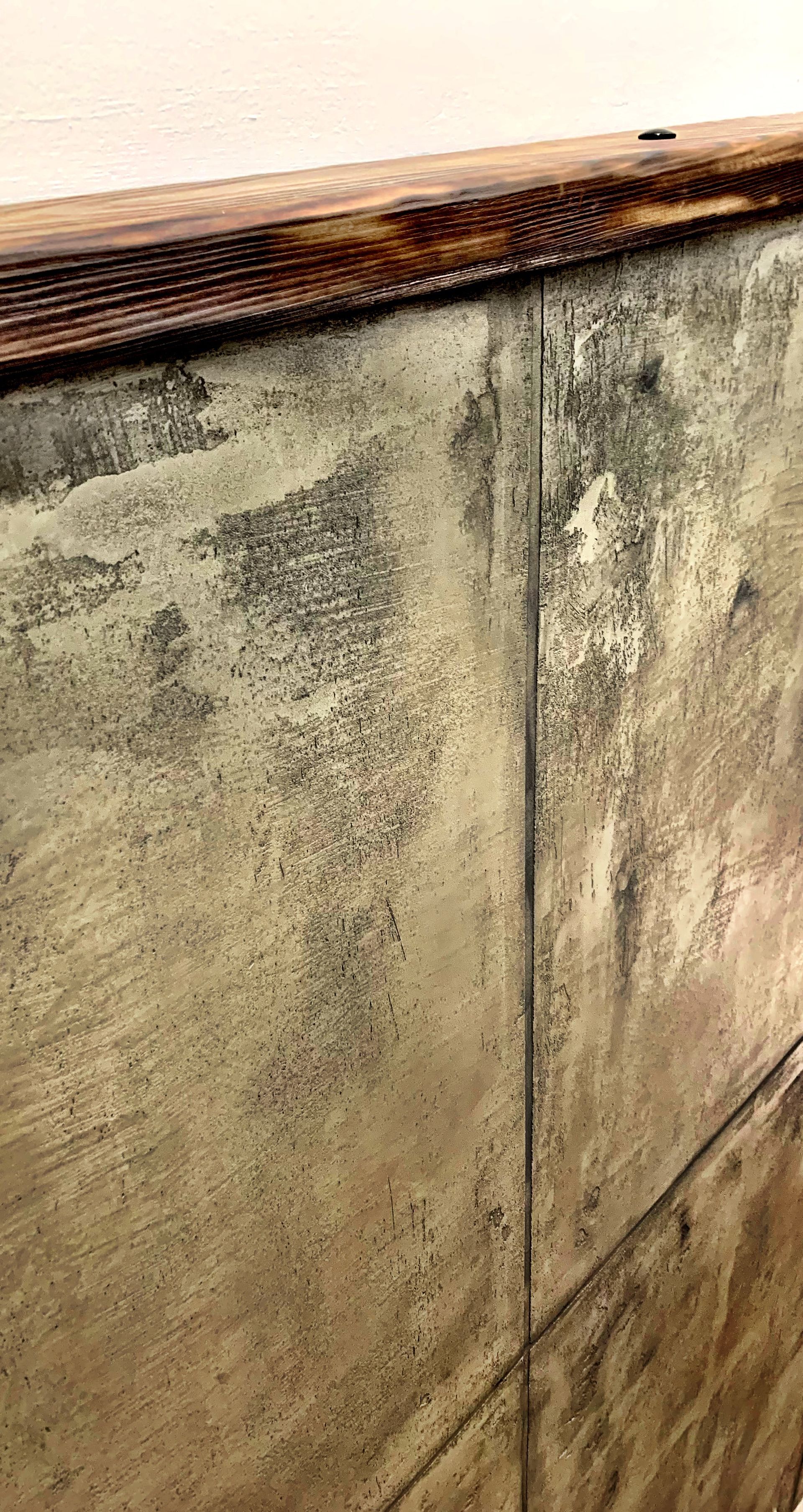 Detailní záběr na omšelou betonovou zeď s dřevěným horním okrajem a viditelnými skvrnami.