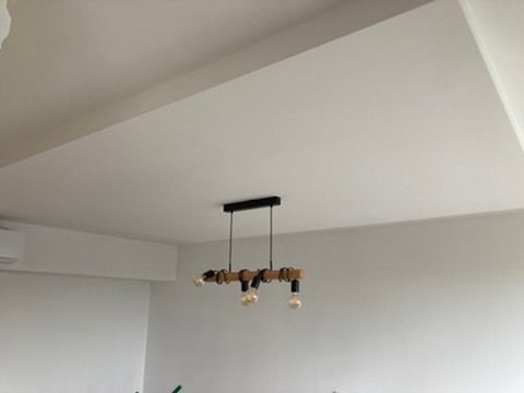 Minimalistický bílý strop s černým závěsným svítidlem a odkrytými žárovkami v místnosti.