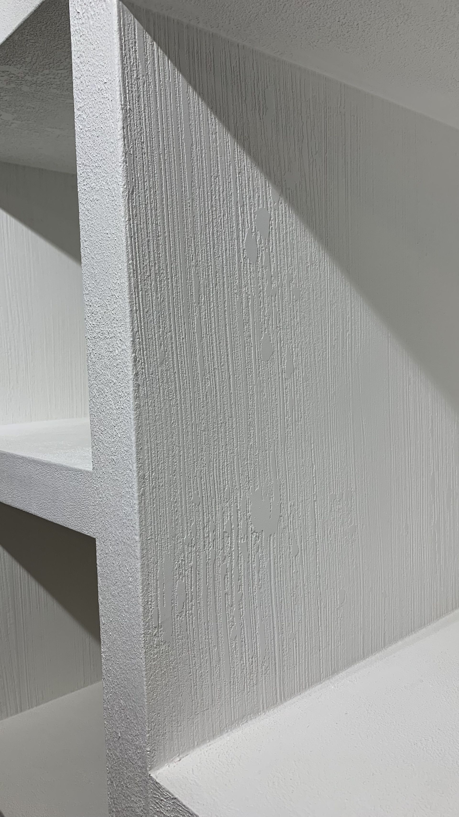 Texturovaná šedobílá geometrická stěna s hranatými stíny a protínajícími se panely