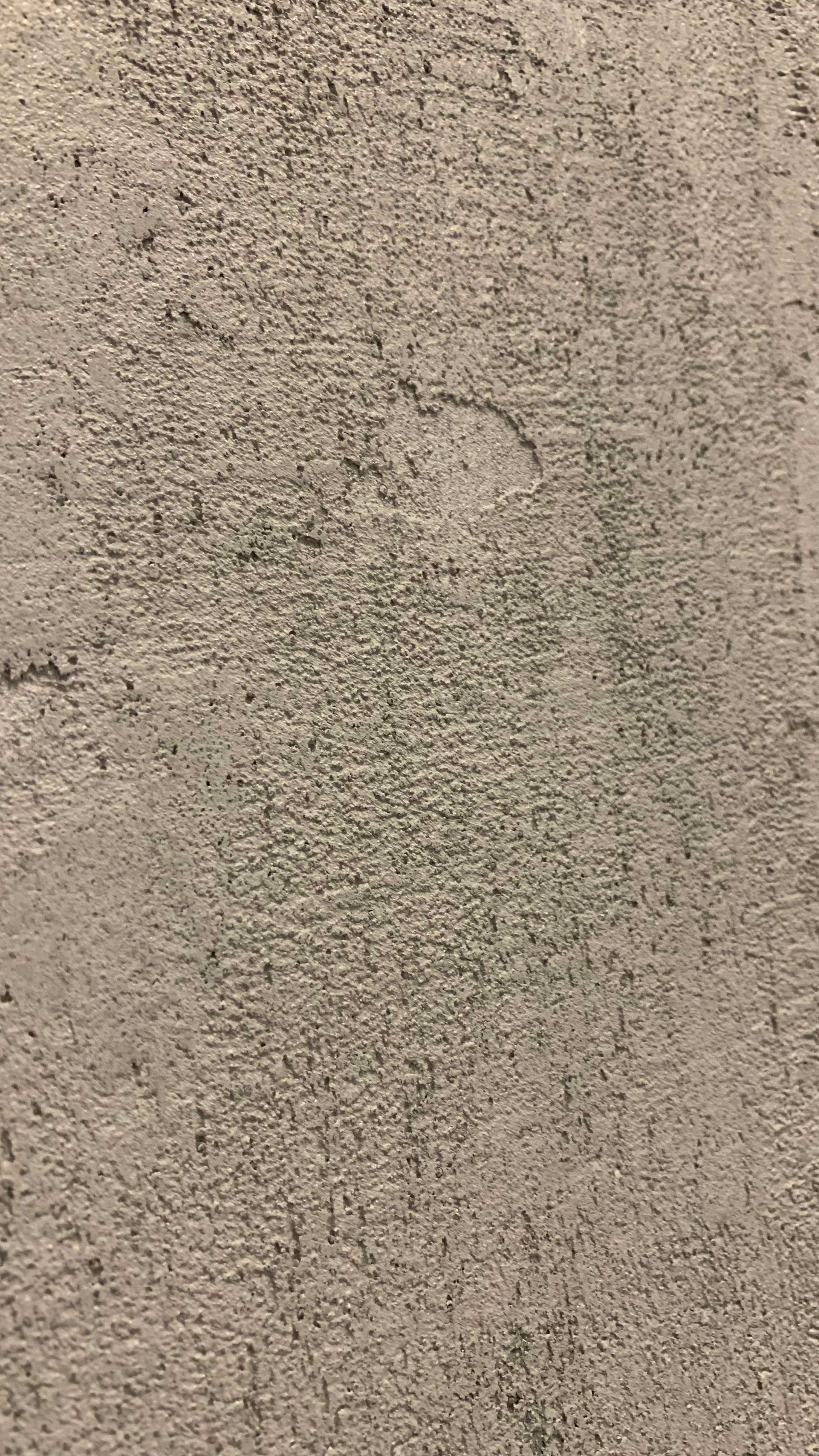 Detail béžové texturované zdi s tmavými skvrnami a slabou svislou značkou