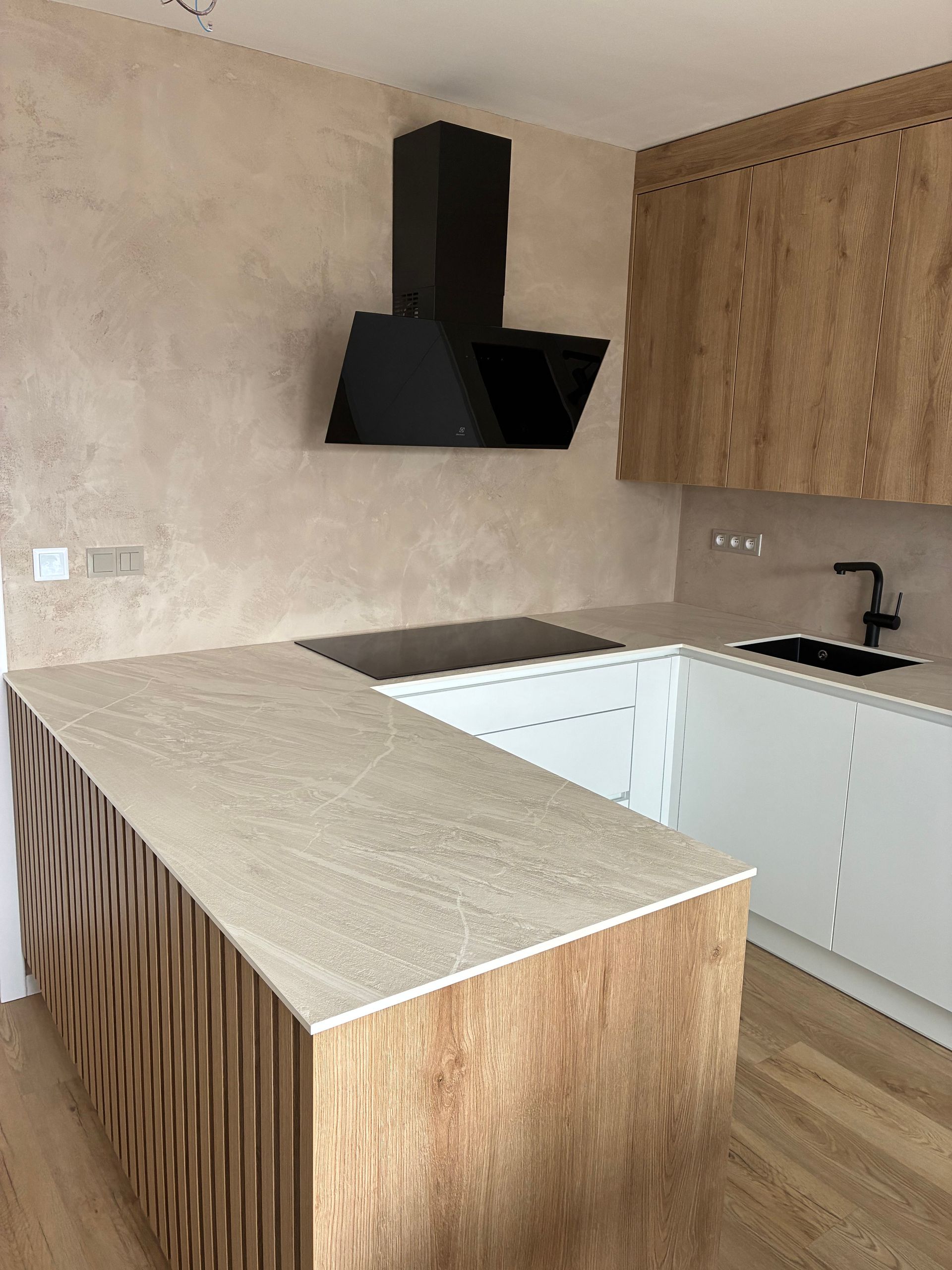 Moderní kuchyně s béžovými skříňkami, bílými deskami a černou digestoří na dřevěné podlaze