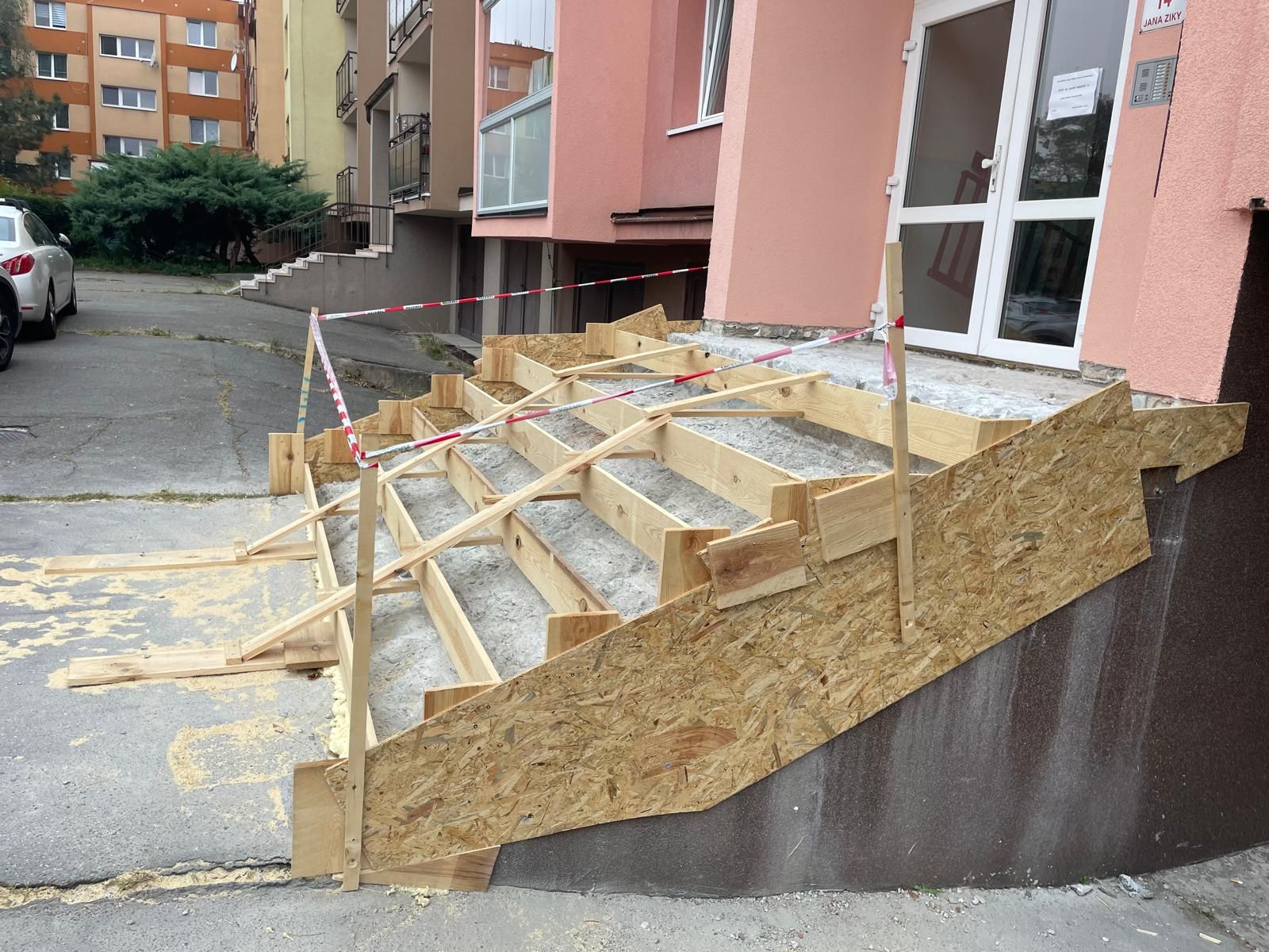 Provizorní překližkové schody a zábradlí vedoucí ke vchodu do budovy na šikmé chodbě