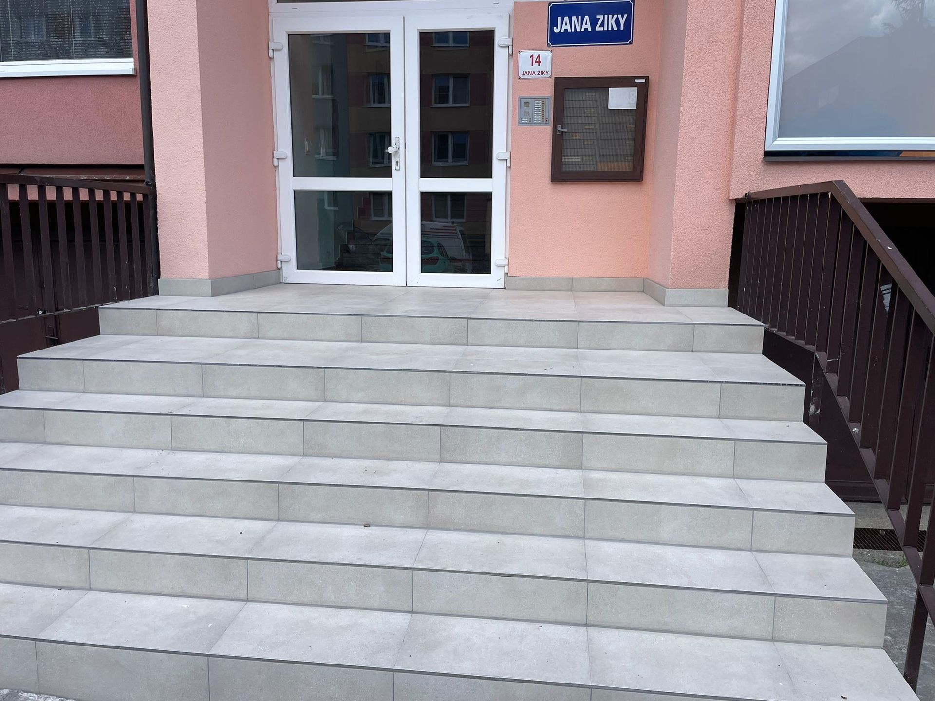Hlavní vchod se širokými betonovými schody, skleněnými dveřmi a nástěnnou poštovní schránkou