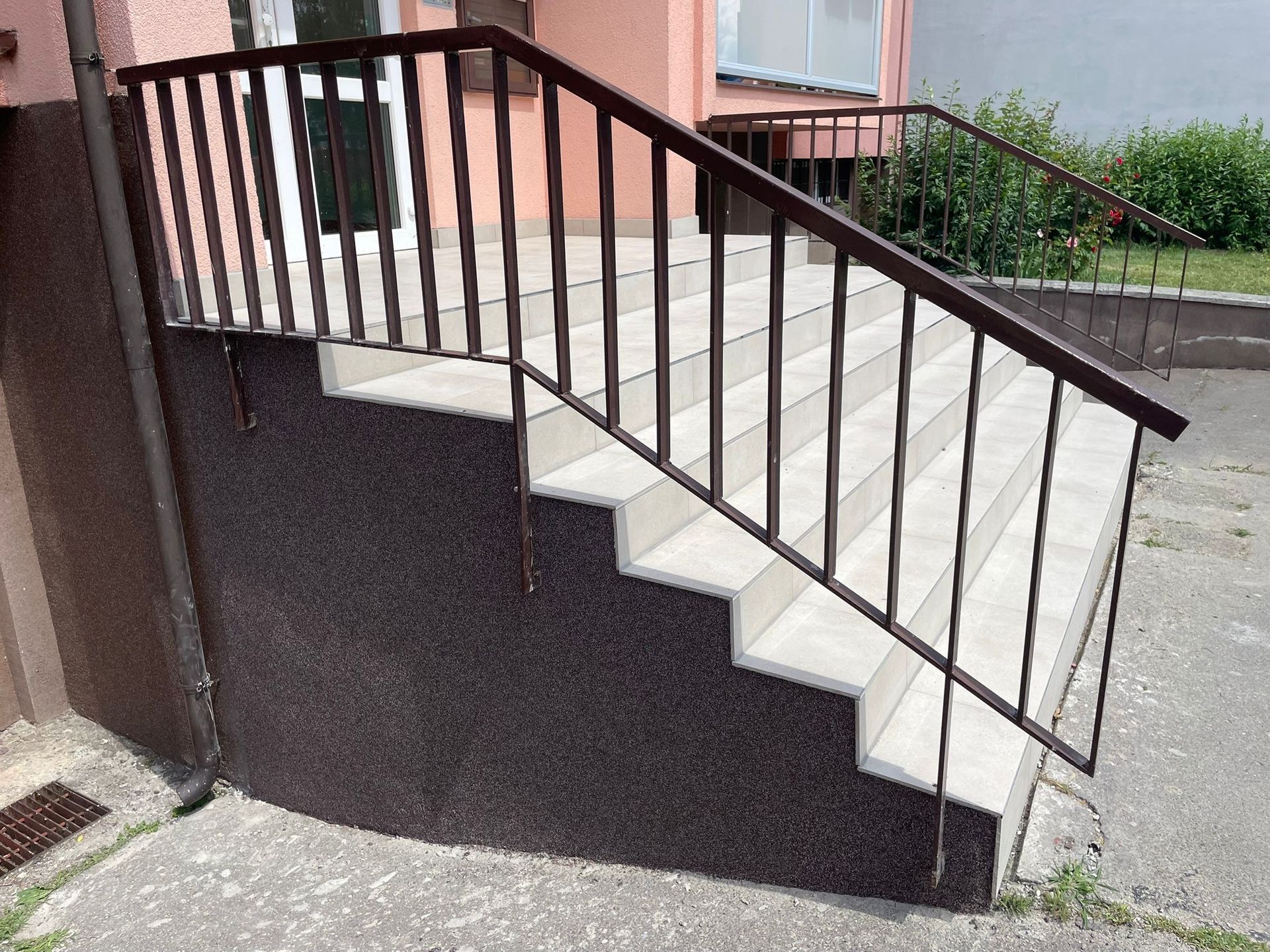 Venkovní betonové schody s tmavým kovovým zábradlím vedle broskvové budovy.