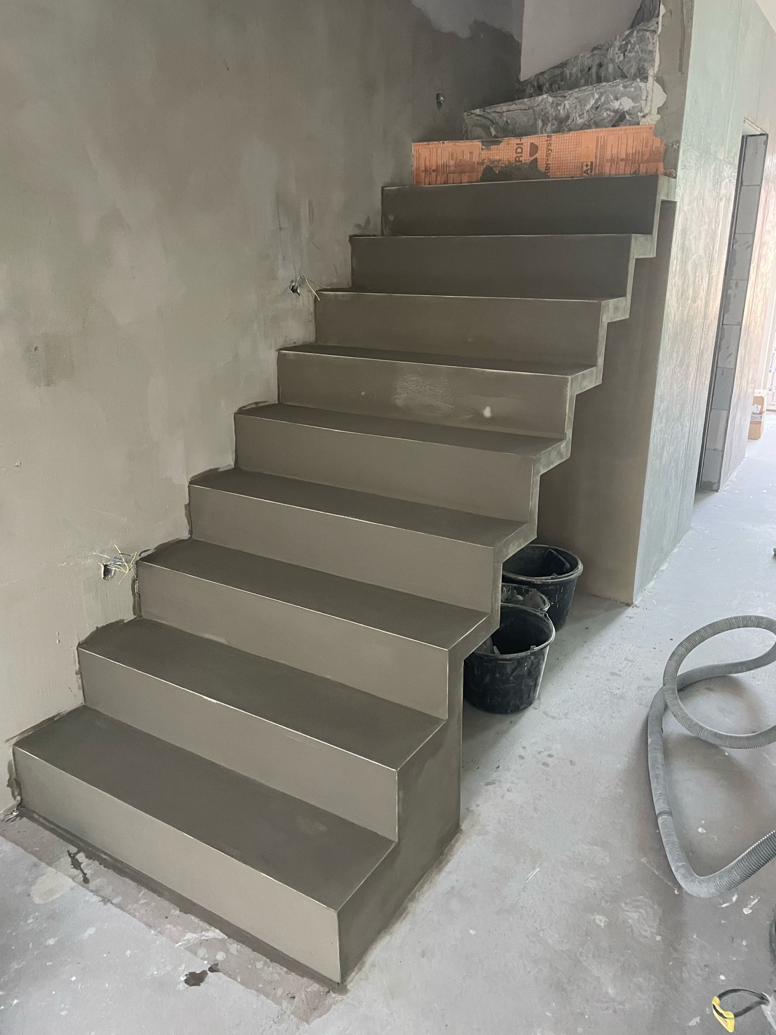 Nedokončené betonové schodiště v úzkém vnitřním schodišti s kbelíky a stavebním materiálem v okolí