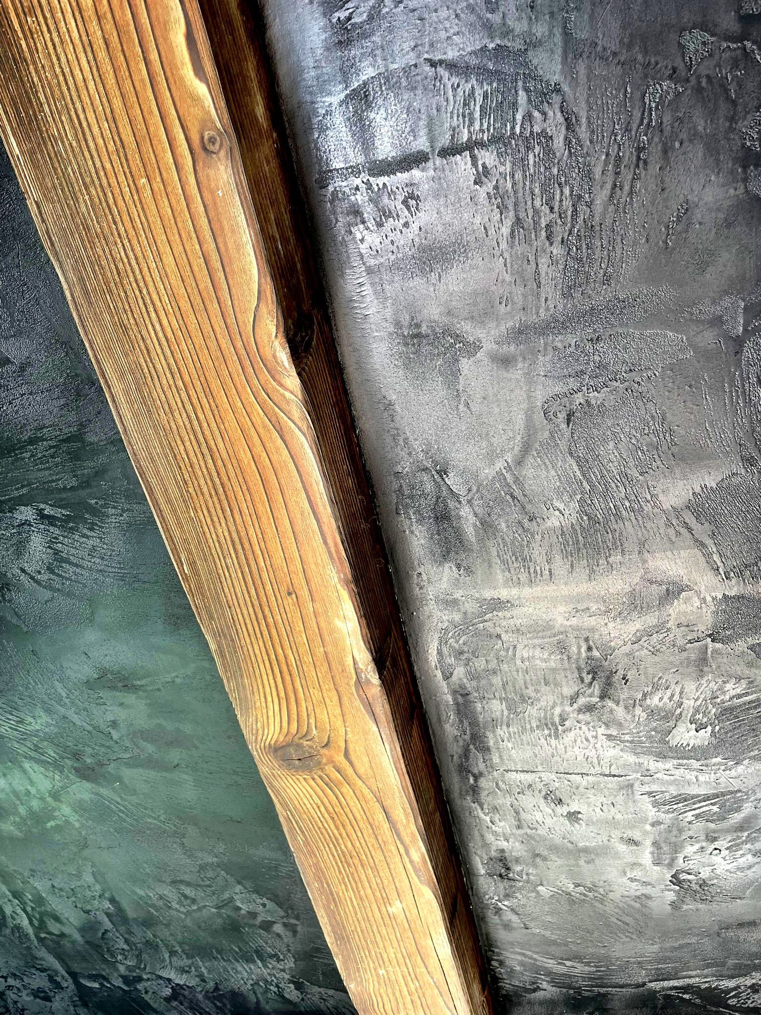 Detail dřevěného trámu vedle šedého, omšelého betonového povrchu.