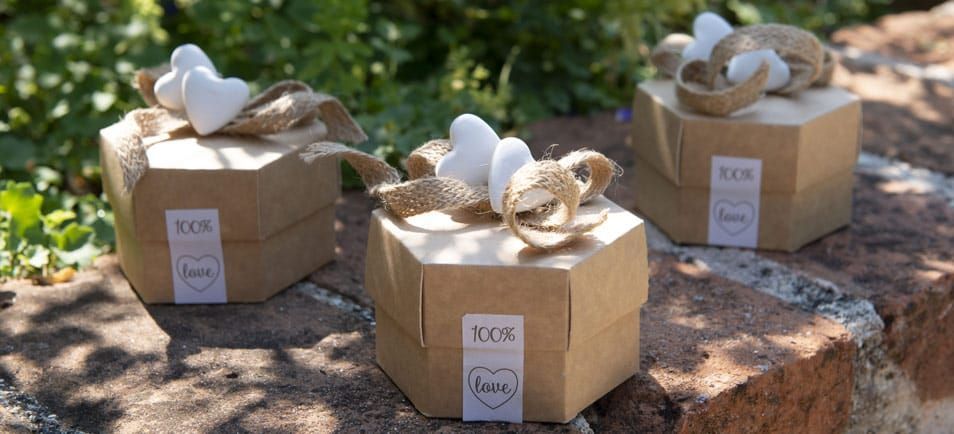Tre scatole esagonali marroni con decorazioni bianche a forma di cuore su una superficie in pietra.