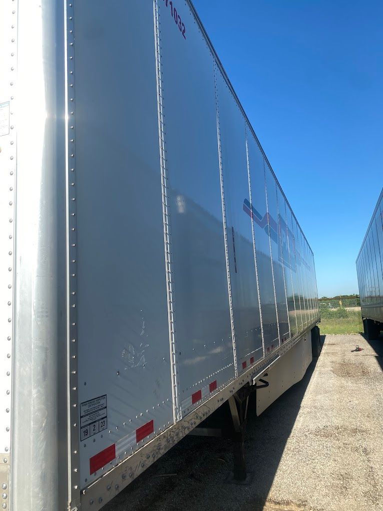 A white trailer is parked in a dirt lot.