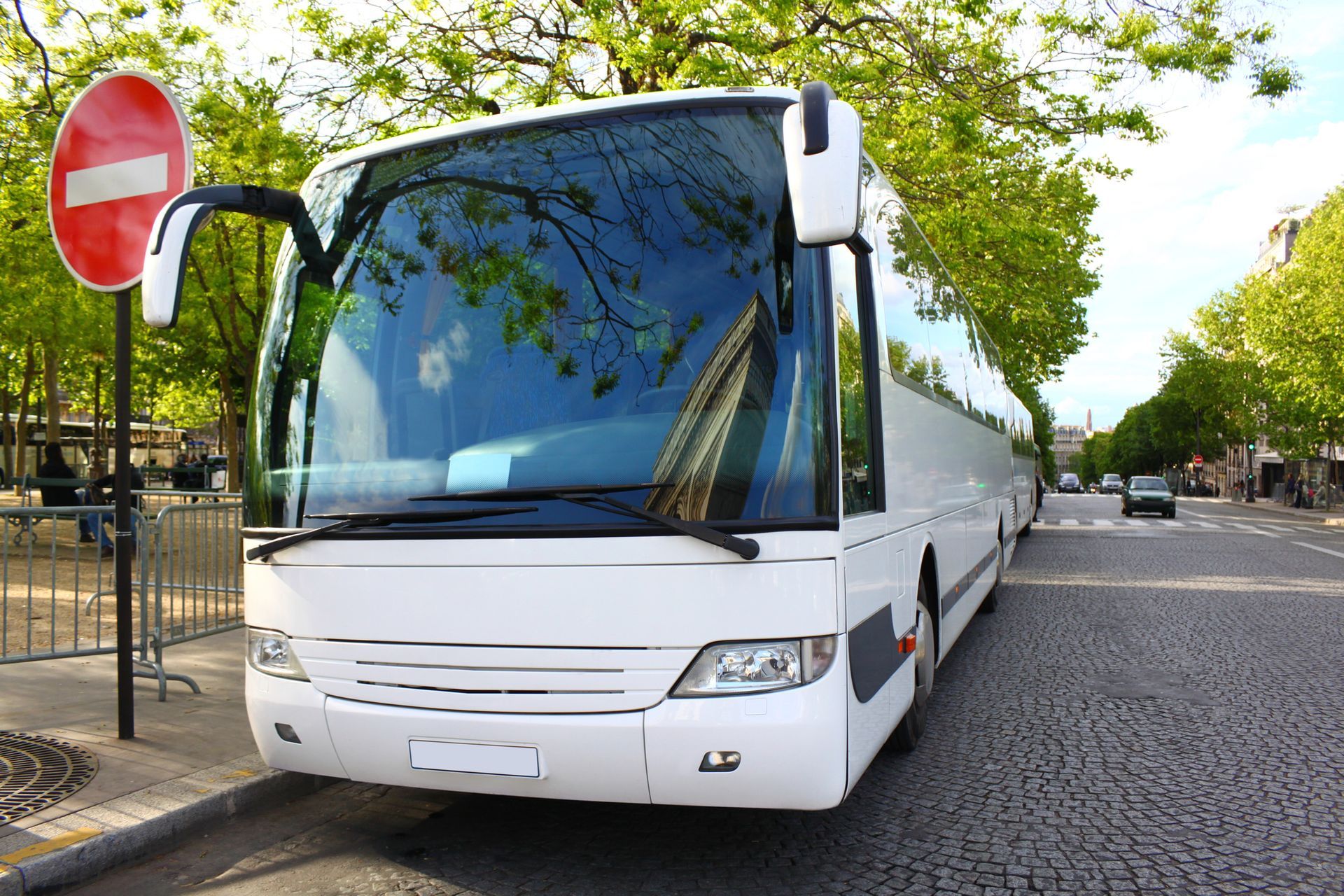 A white bus is parked on the side of the road next to a no entry sign.