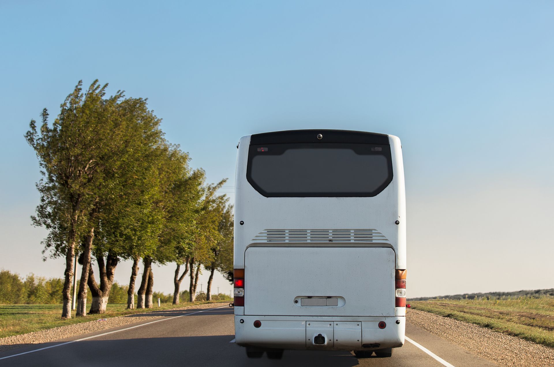 A white bus is driving down a country road.