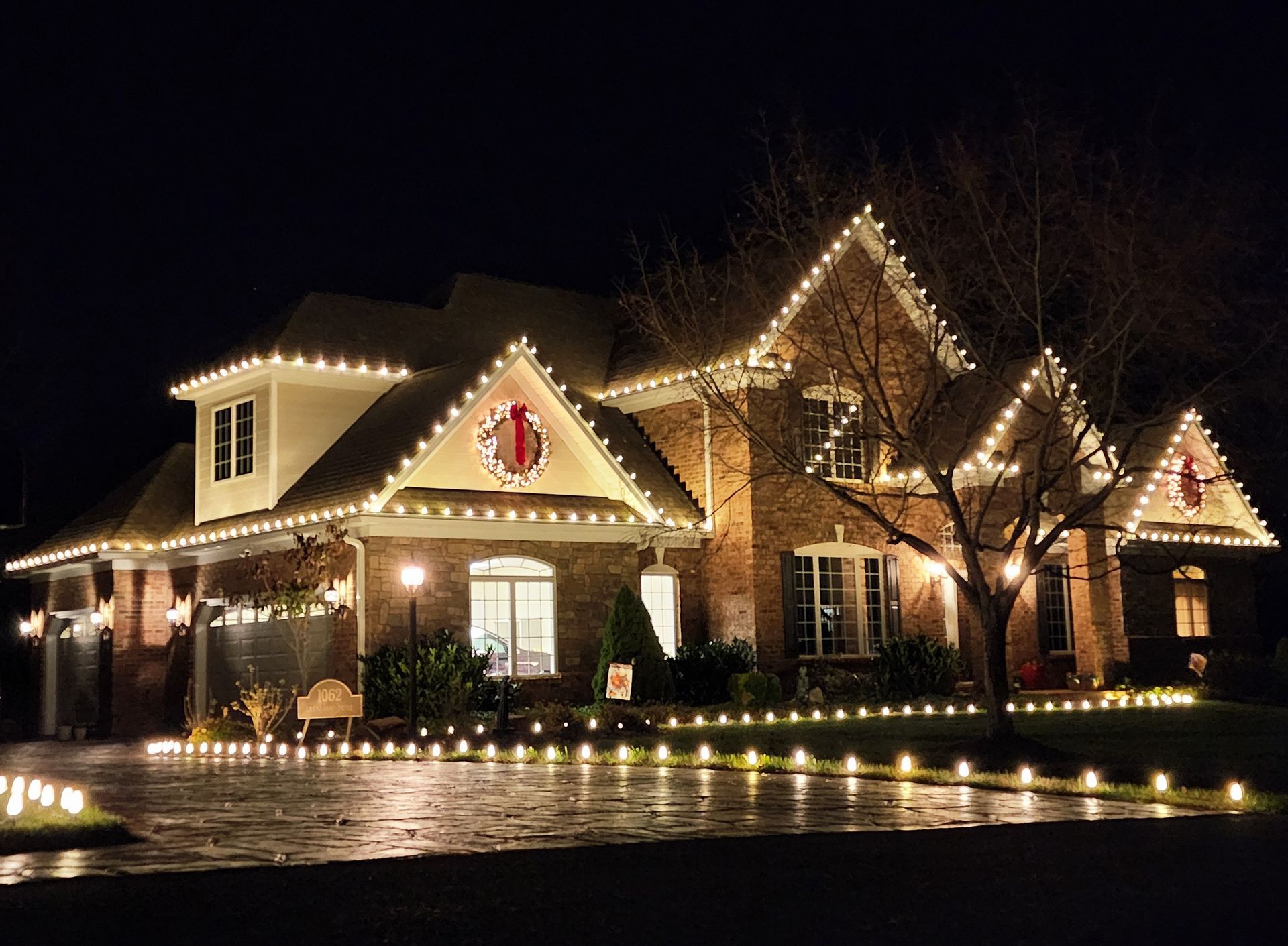 House and landscaping brightly illuminated with white Christmas lights at night.