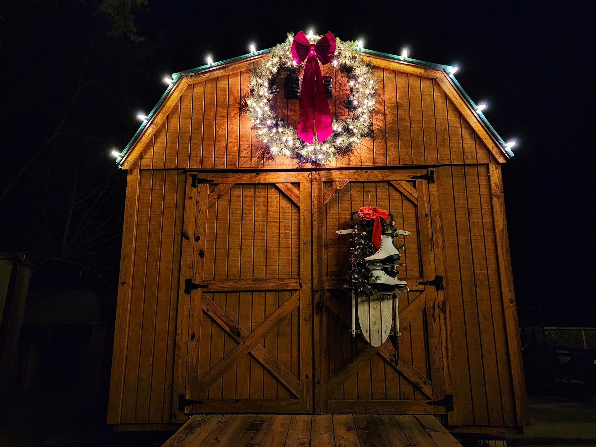 Wooden shed decorated for Christmas with wreath and lights.